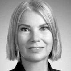 Czarno-biały portret kobiety z prostymi, jasnymi włosami przyciętymi na boba, ubranej w ciemną bluzkę, lekko uśmiechniętej i patrzącej bezpośrednio w obiektyw.